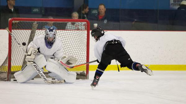 Teenage girl player using dryland pucks with PassMaster on shooting pad and about to shoot towards shooting tarp, while teenage boy player uses stickhandling balls with SweetHands stickhandling aid