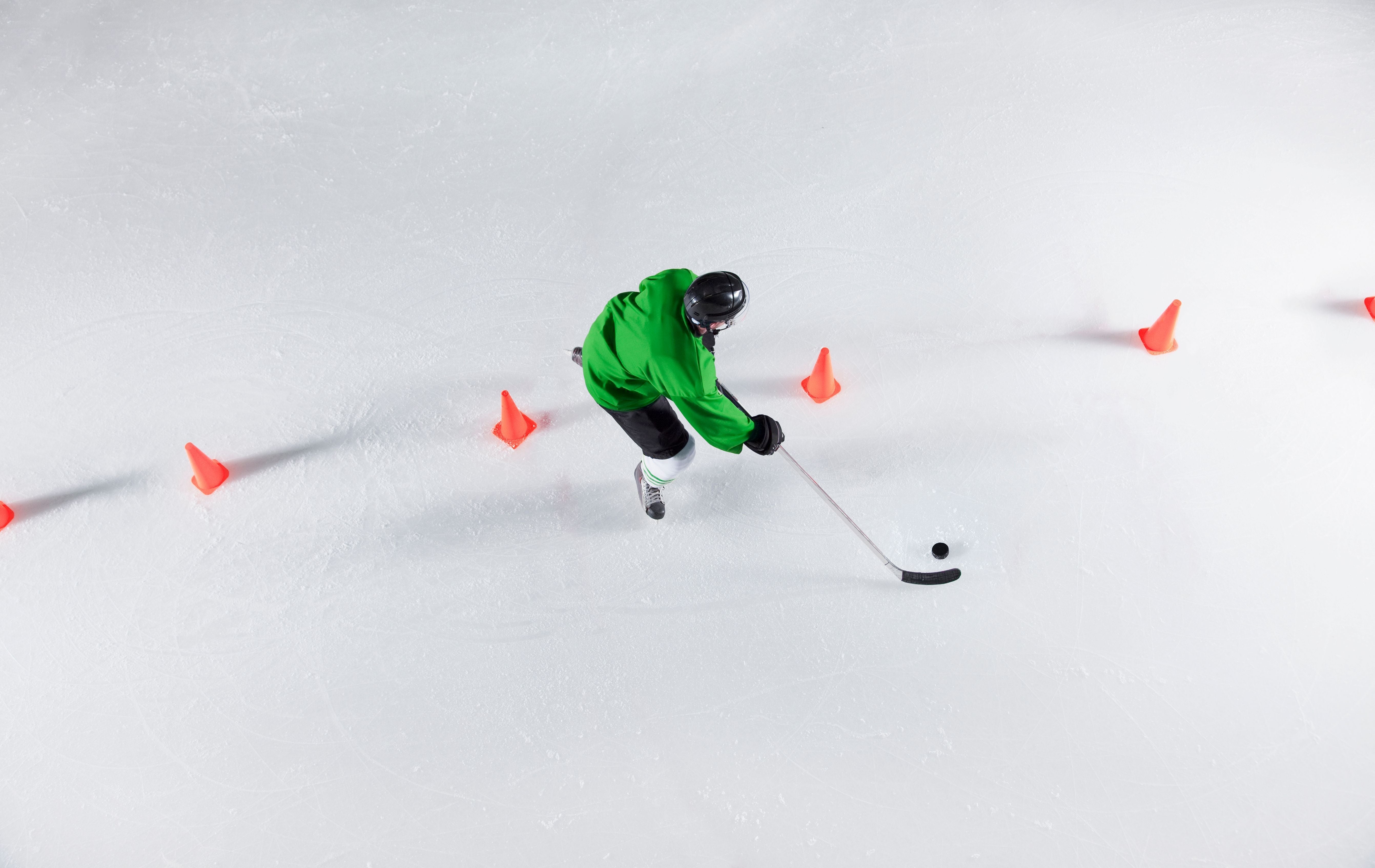 Ice hockey player in green jersey skating around cones 