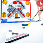A person practicing hockey drills with a green and black PASSMASTER hockey training aid on an ice rink.