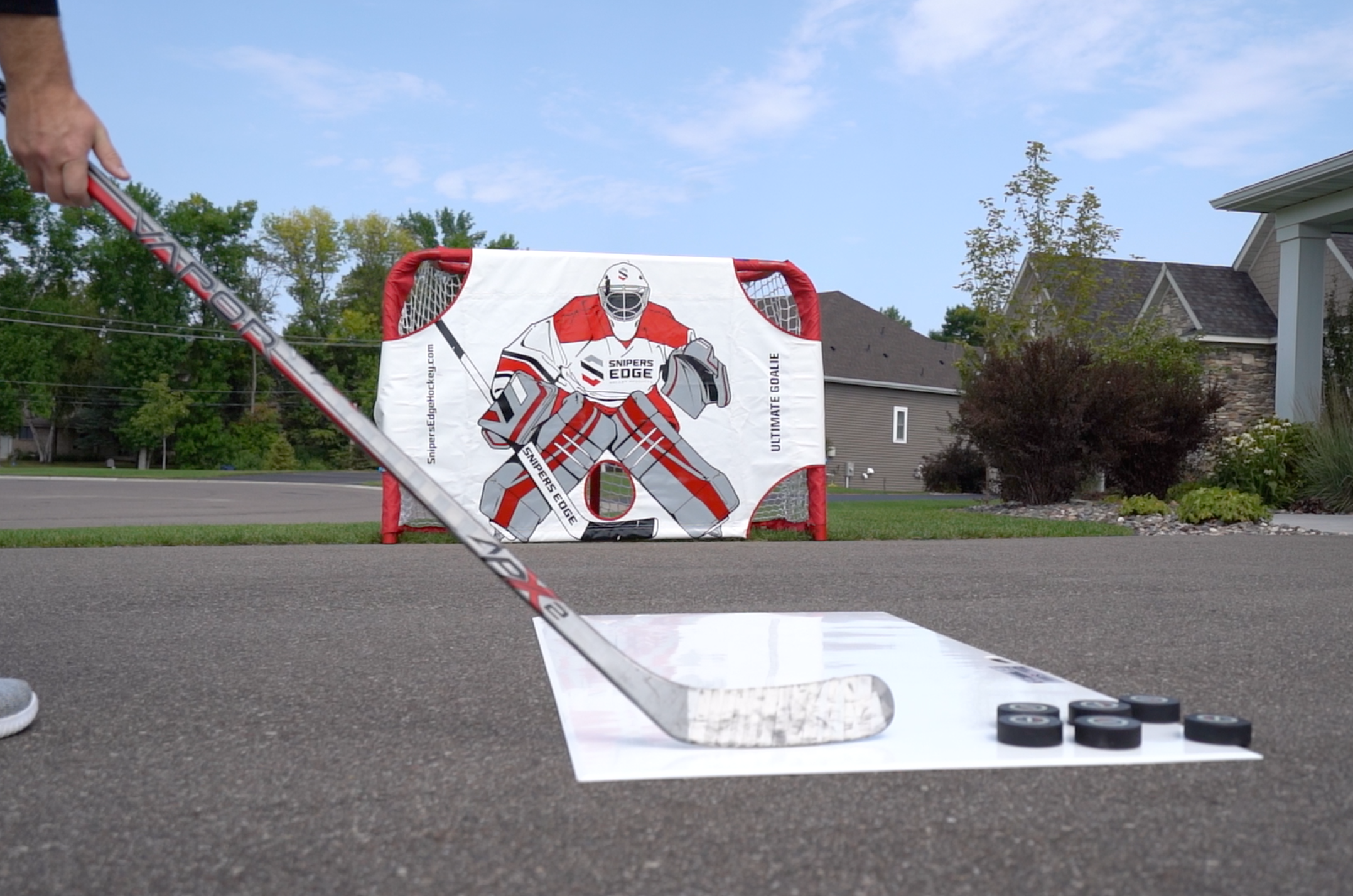 Player shooting pucks on driveway, using shooting pad and ultimate goalie