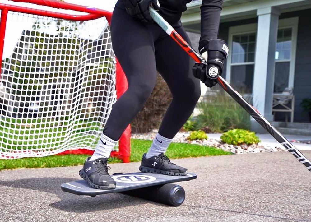 a player balancing on the balance board with a hockey stick in a driveway